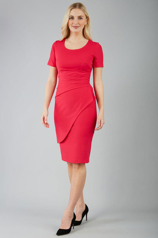 A model wearing a red knee-length pencil dress with short sleeves and a round neckline, featuring cross-body pleating and an overlaid skirt in virtual pink colour