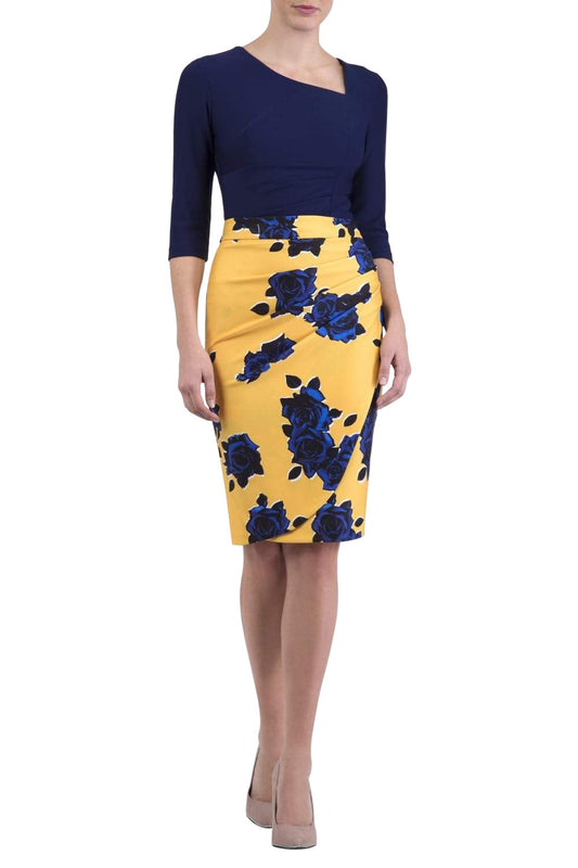 Woman wearing a navy top and yellow floral skirt on a city street.