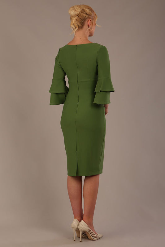 A woman wearing a vineyard green knee-length diva catwalk meridian pencil dress with a round neckline, double layered peplum three quarter length sleeves, and standing against a plain background.