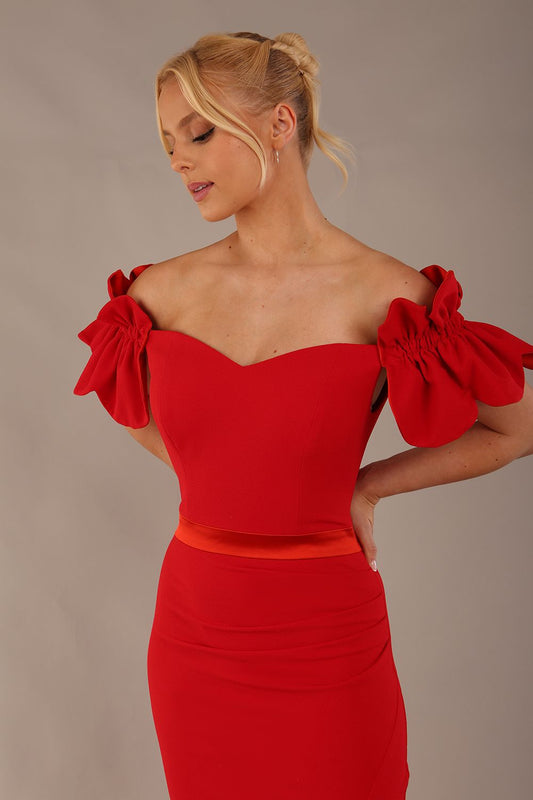 Woman wearing a red dress with ruffled sleeves in an elegant indoor setting. (Passion Red & Fire Orange Satin)