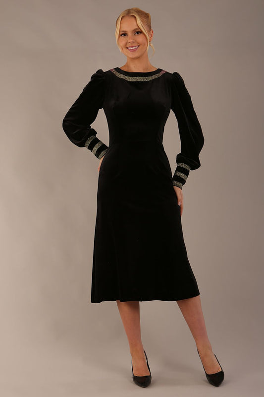 Woman wearing a black dress with gold accents sitting on a stool against a beige background (Black Velvet with Sherwood Glitter Contrast)