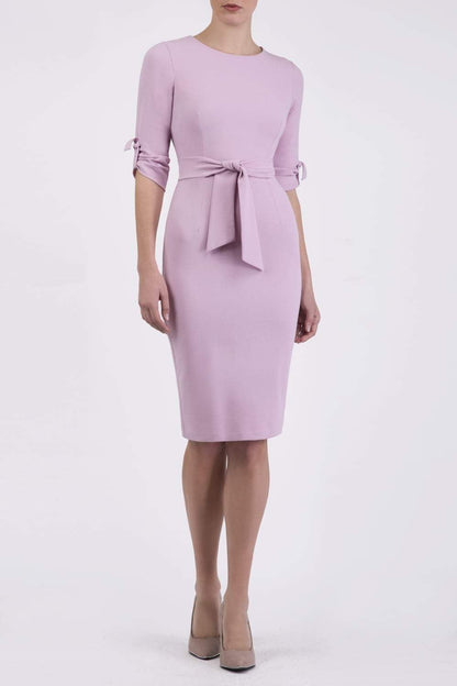 brunette model wearing diva catwalk tryst pencil dawn pink dress with sleeves and belt detail at the front with rounded neckline front