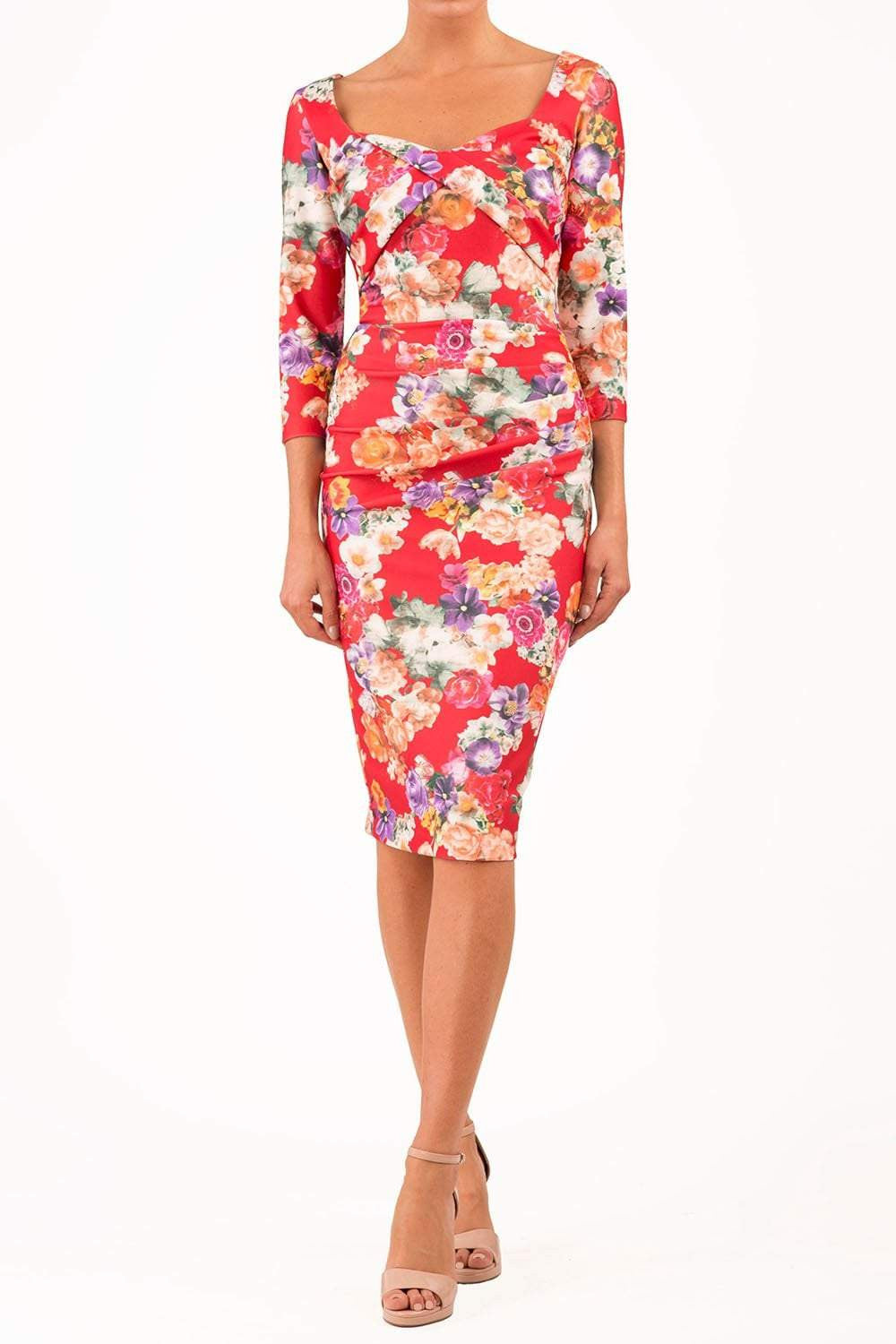 A model wearing a red floral satin stretch fabric dress with a semi-sweetheart neckline, three-quarter length sleeves, and a concealed zip at the back. The dress features pleating detail at the front.