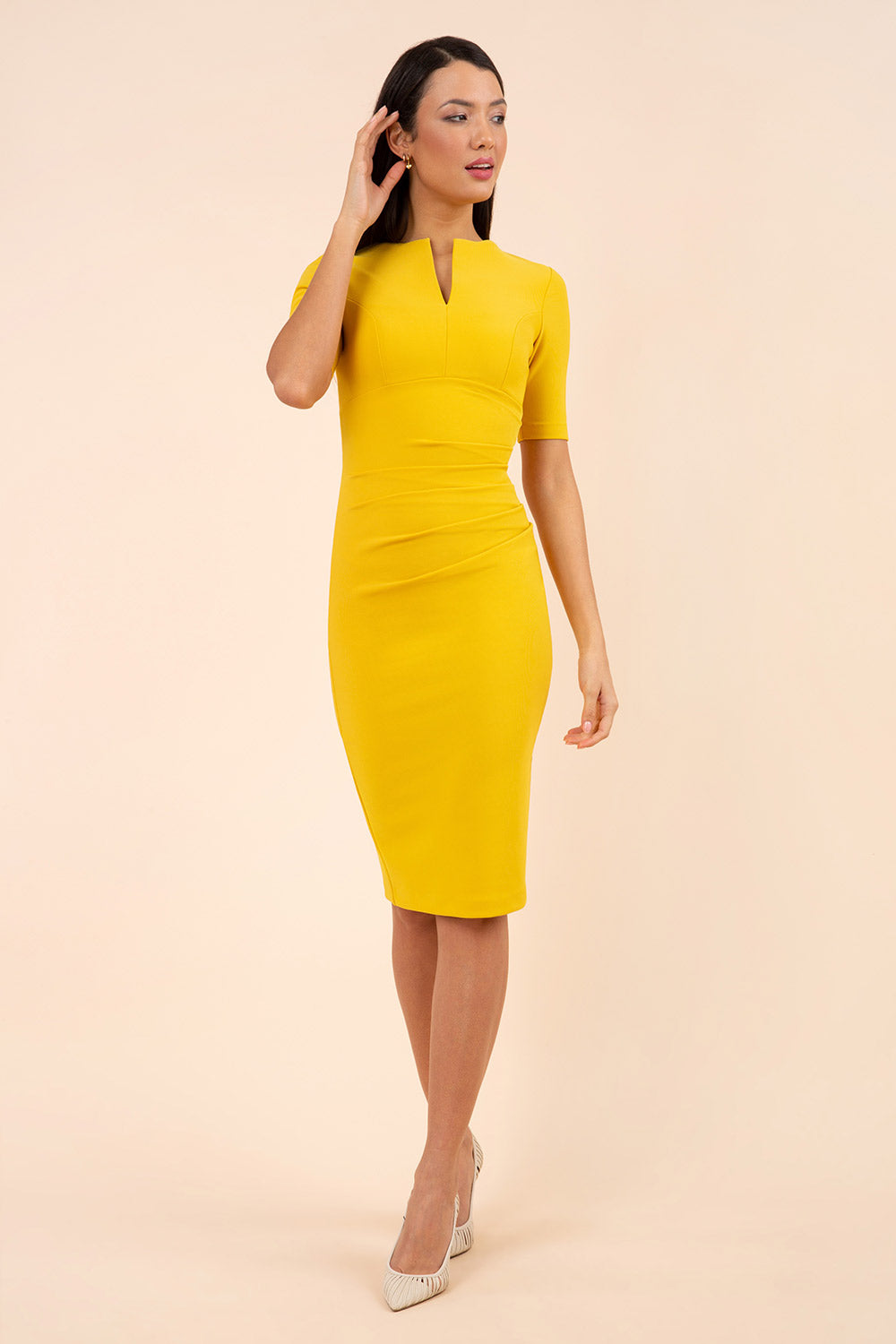 blonde model is wearing diva catwalk lydia short sleeve pencil fitted dress in mustard yellow colour with rounded neckline with a slit in the middle front