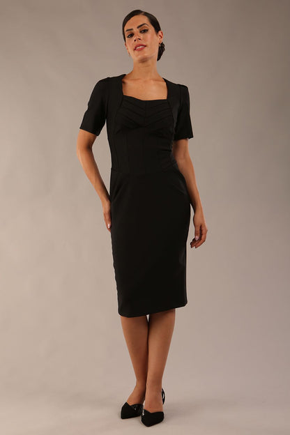 model wearing seed belgravia square neckline pencil dress with short pleated sleeves and folded pleating at the front in black colour