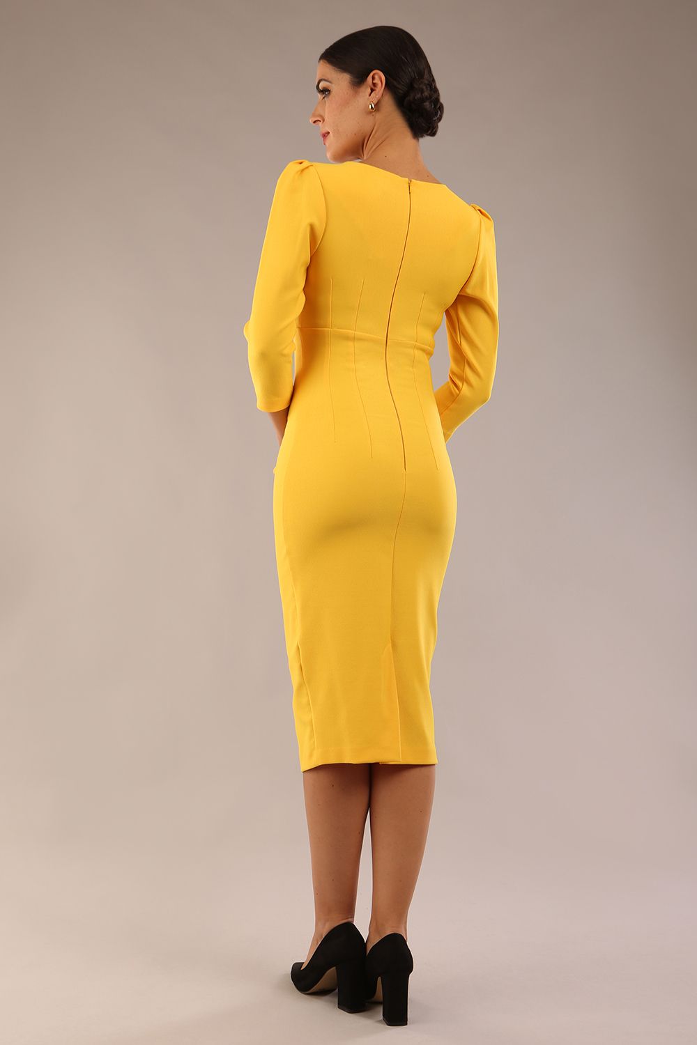 model is wearing a diva catwalk seed fitzrovia 3/4 sleeve pencil dress with round neckline and v-slit and pleating details on the skirt in daffodil yellow front
