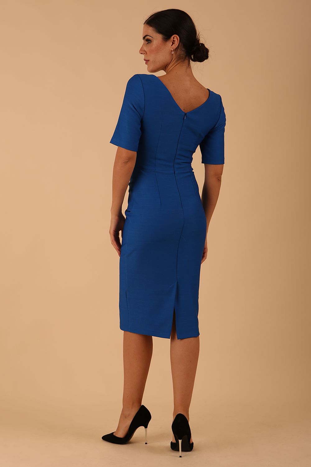 model wearing diva catwalk couture wiltshire fitted pencil-skirt dress with short sleeves and open v-neckline and pleating across the tummy area in sapphire blue colour front