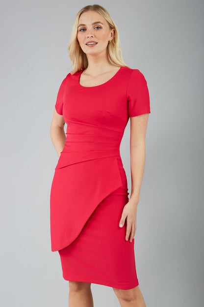 A model wearing a red knee-length pencil dress with short sleeves and a round neckline, featuring cross-body pleating and an overlaid skirt in virtual pink colour