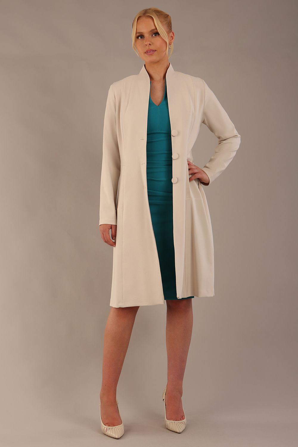 blonde model wearing diva catwalk couture fine raquella coat with buttons across the front and long sleeves with high neck and pockets in sandy cream colour front (Sandy Cream)