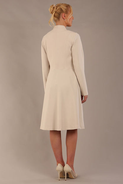 blonde model wearing diva catwalk couture fine raquella coat with buttons across the front and long sleeves with high neck and pockets in sandy cream colour front (Sandy Cream)