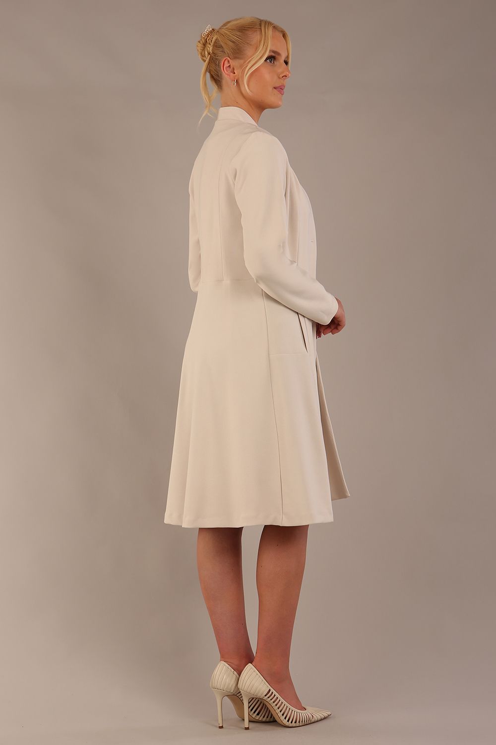 blonde model wearing diva catwalk couture fine raquella coat with buttons across the front and long sleeves with high neck and pockets in sandy cream colour front (Sandy Cream)