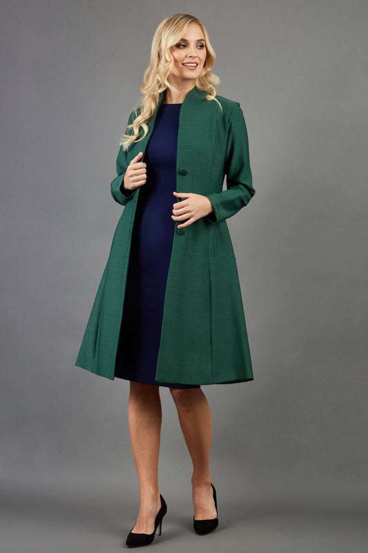 blonde model wearing diva catwalk couture fine raquella coat with buttons across the front and long sleeves with high neck and pockets in chrome green colour front (Chrome Green)