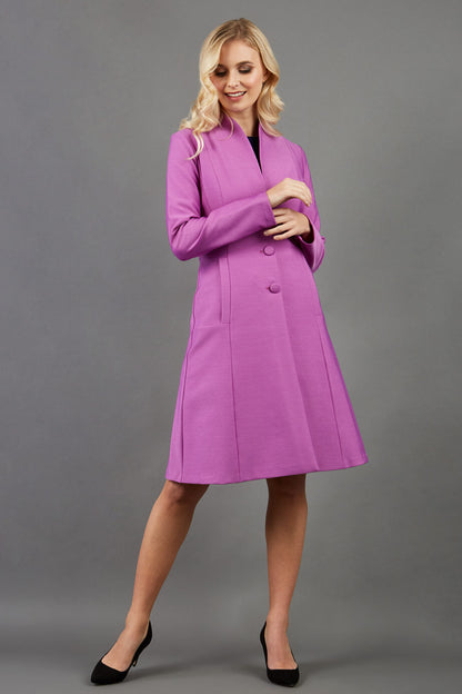 blonde model wearing diva catwalk couture fine raquella coat with buttons across the front and long sleeves with high neck and pockets in magenta mist colour front (Magenta Mist)