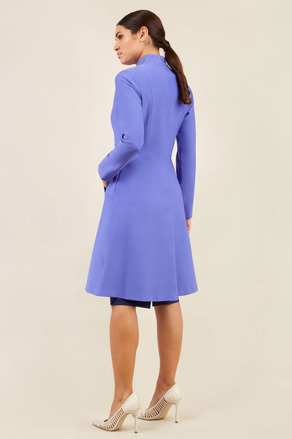 brunette model wearing diva catwalk couture fine raquella coat with buttons across the front and long sleeves with high neck and pockets in fusion indigo colour front (Dawn Indigo)