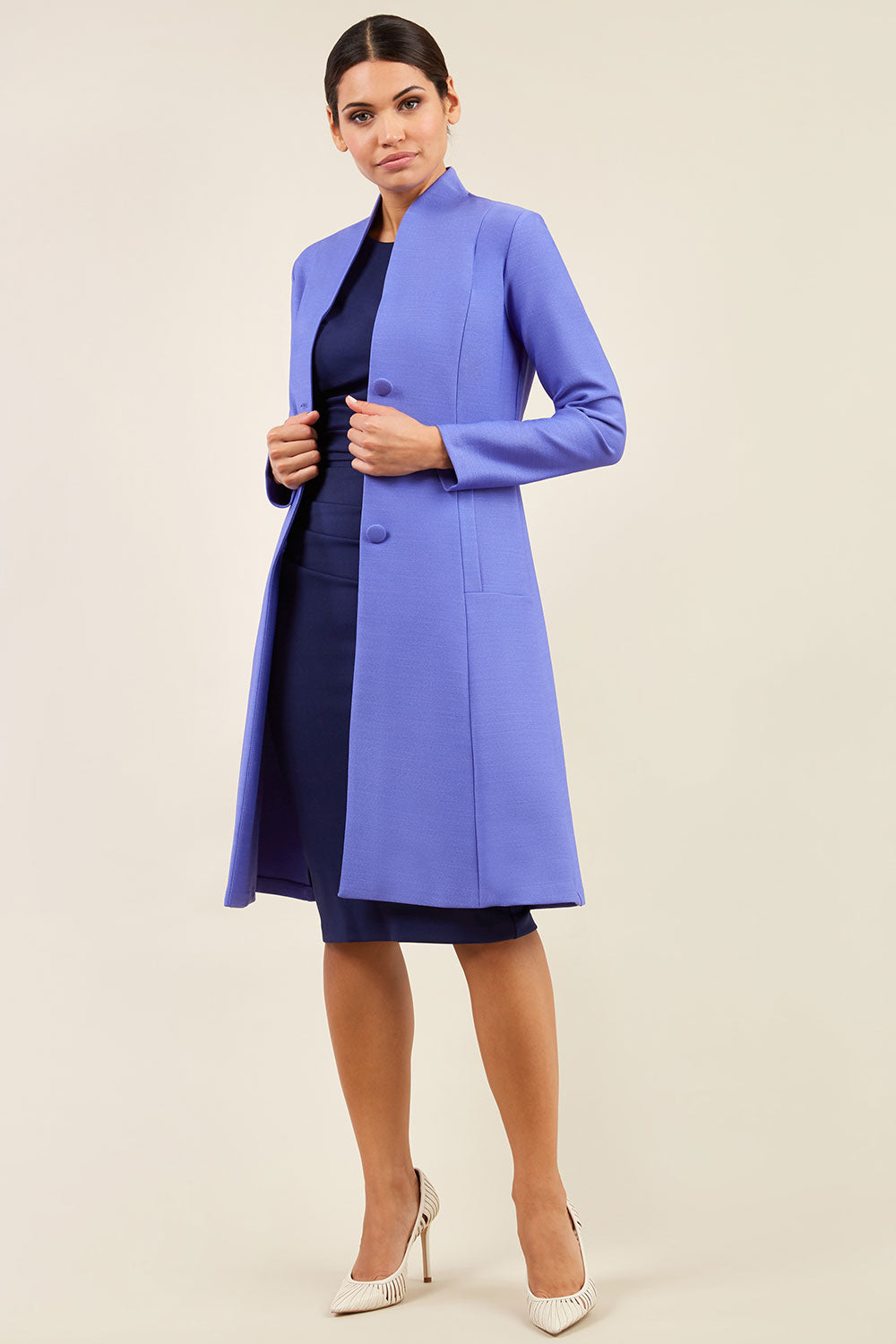 brunette model wearing diva catwalk couture fine raquella coat with buttons across the front and long sleeves with high neck and pockets in fusion indigo colour front (Dawn Indigo)
