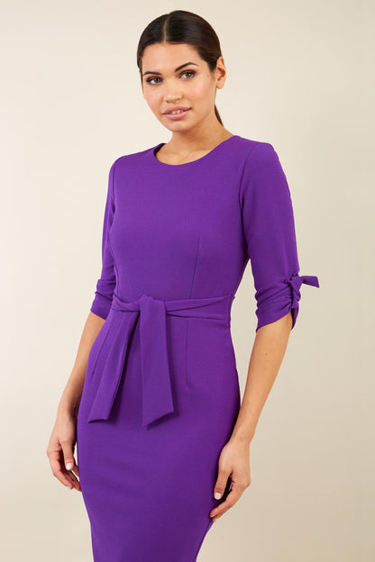brunette model wearing diva catwalk tryst pencil purple dress with sleeves and belt detail at the front with rounded neckline front