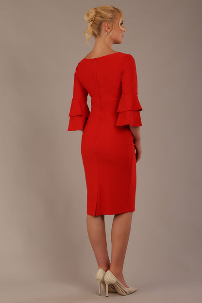 A woman wearing a electric red knee-length diva catwalk meridian pencil dress with a round neckline, double layered peplum three quarter length sleeves, and standing against a plain background.
