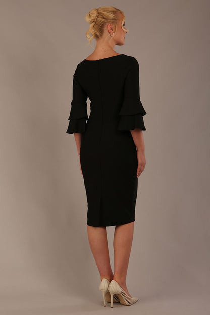 A woman wearing a black knee-length diva catwalk meridian pencil dress with a round neckline, double layered peplum three quarter length sleeves, and standing against a plain background.
