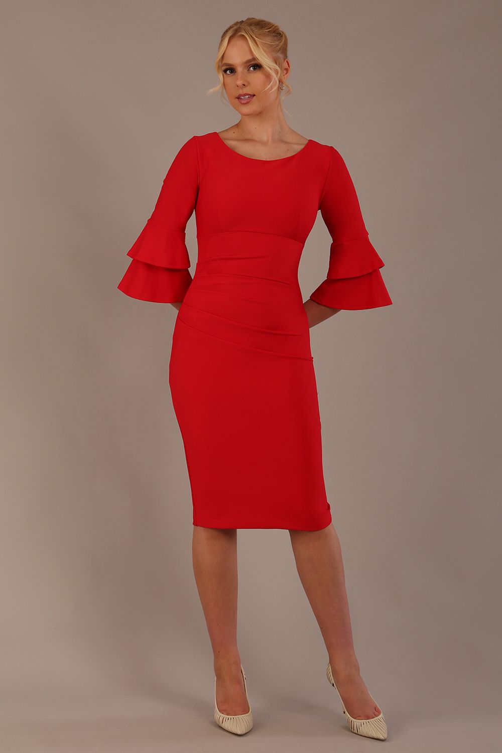 A woman wearing a electric red knee-length diva catwalk meridian pencil dress with a round neckline, double layered peplum three quarter length sleeves, and standing against a plain background.