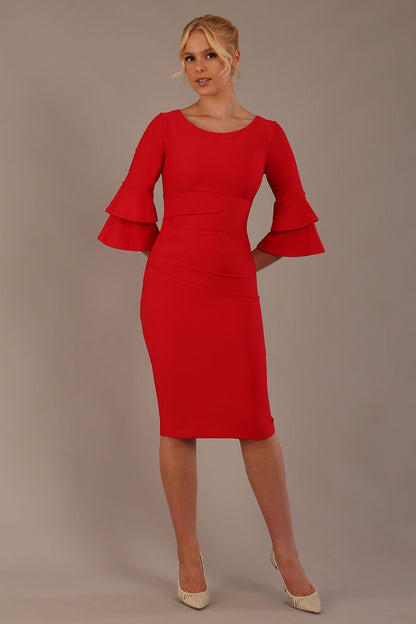 A woman wearing a electric red knee-length diva catwalk meridian pencil dress with a round neckline, double layered peplum three quarter length sleeves, and standing against a plain background.