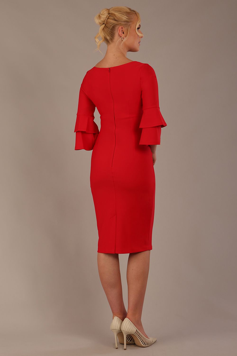 A woman wearing a electric red knee-length diva catwalk meridian pencil dress with a round neckline, double layered peplum three quarter length sleeves, and standing against a plain background.
