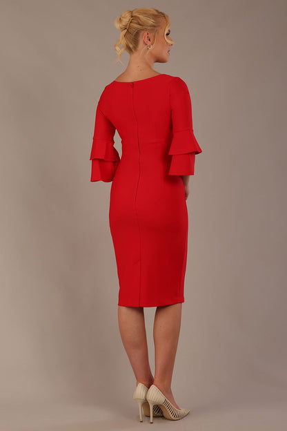 A woman wearing a electric red knee-length diva catwalk meridian pencil dress with a round neckline, double layered peplum three quarter length sleeves, and standing against a plain background.