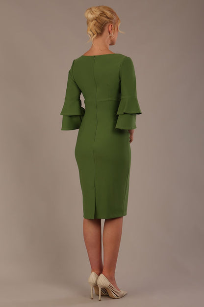 A woman wearing a vineyard green knee-length diva catwalk meridian pencil dress with a round neckline, double layered peplum three quarter length sleeves, and standing against a plain background.