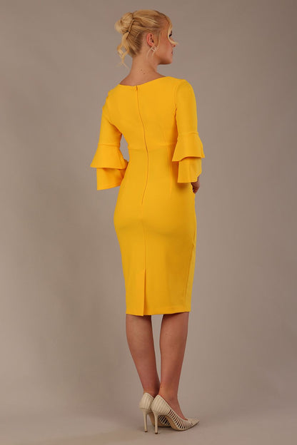A woman wearing a sunshine yellow knee-length diva catwalk meridian pencil dress with a round neckline, double layered peplum three quarter length sleeves, and standing against a plain background.