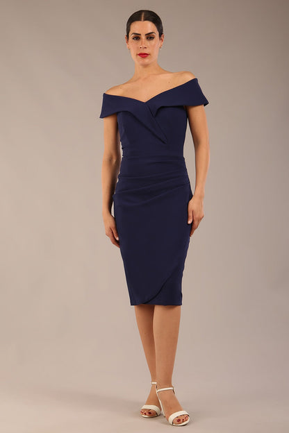 brunette model wearing diva catwalk pencil skirt dress sleeveless with lowered neckline and pleating on side in navy blue colour front image