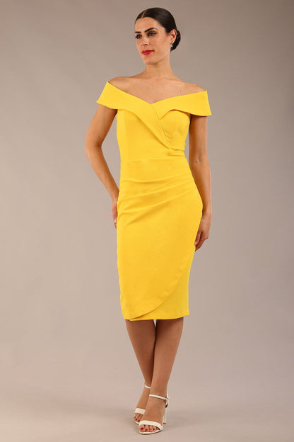 brunette model wearing diva catwalk pencil skirt dress sleeveless with lowered neckline and pleating on side in freesia yellow colour front image