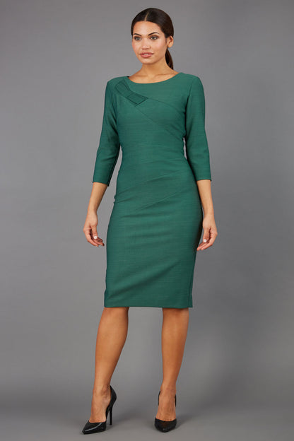 brunette model wearing diva catwalk couture althorp pencil fitted dress with sleeves and rounded neckline and bow detail at the top in chrome green colour front