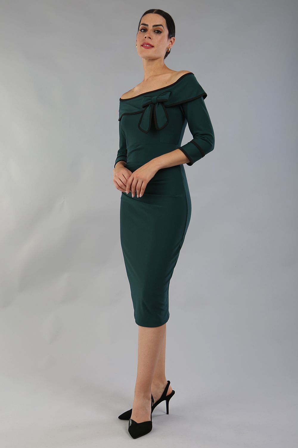 model wearing a diva catwalk Paige Bi-Stretch Dress with 3/4 sleeve, knee length, Fold over off-shoulder neckline with bow detail and with Contrast piping on sleeve cuffs and neckline in Forest Green and black colour