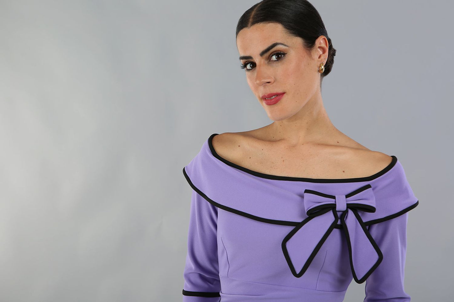 model wearing a diva catwalk Paige Bi-Stretch Dress with 3/4 sleeve, knee length, Fold over off-shoulder neckline with bow detail and with Contrast piping on sleeve cuffs and neckline in Lilac Wisteria and black colour