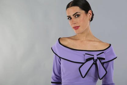 model wearing a diva catwalk Paige Bi-Stretch Dress with 3/4 sleeve, knee length, Fold over off-shoulder neckline with bow detail and with Contrast piping on sleeve cuffs and neckline in Lilac Wisteria and black colour