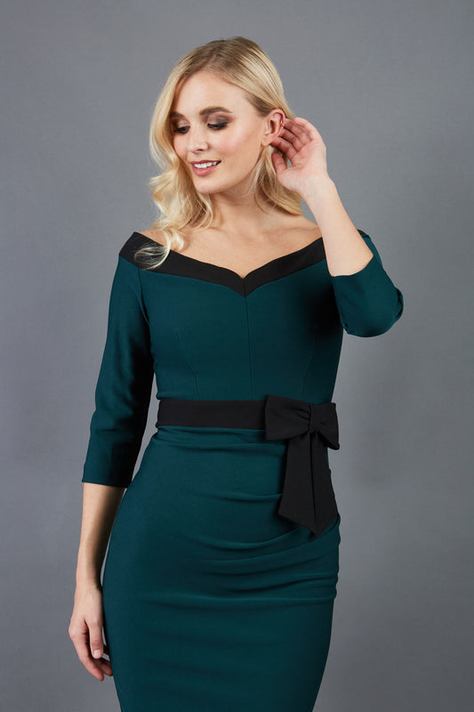 blonde model wearing diva catwalk luma pencil skirt dress with contrasting bow off shoulder with sleeves in forest green front
