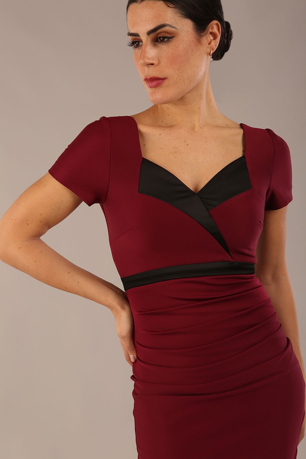 model is wearing a diva catwalk dress in burgundy with black satin detail contrast on the neckline and waistband short sleeves and pleating details with knee length