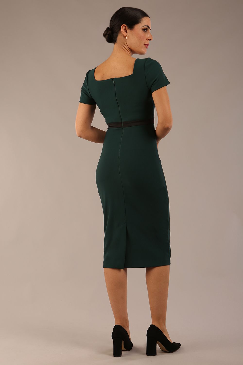 model is wearing a diva catwalk dress in forest green with black satin detail contrast on the neckline and waistband short sleeves and pleating details with knee-length back