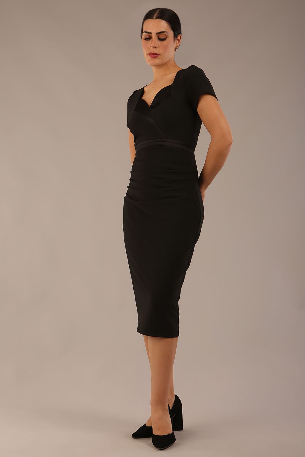 model is wearing a diva catwalk dress in black with black satin detail contrast on the neckline and waistband short sleeves and pleating details with knee length