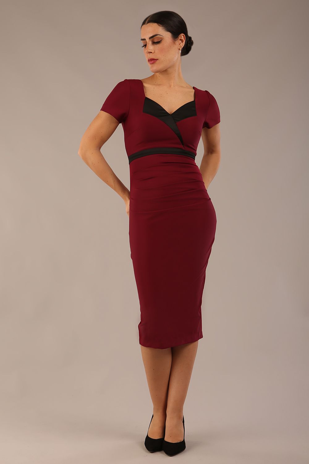 model is wearing a diva catwalk dress in burgundy with black satin detail contrast on the neckline and waistband short sleeves and pleating details with knee length