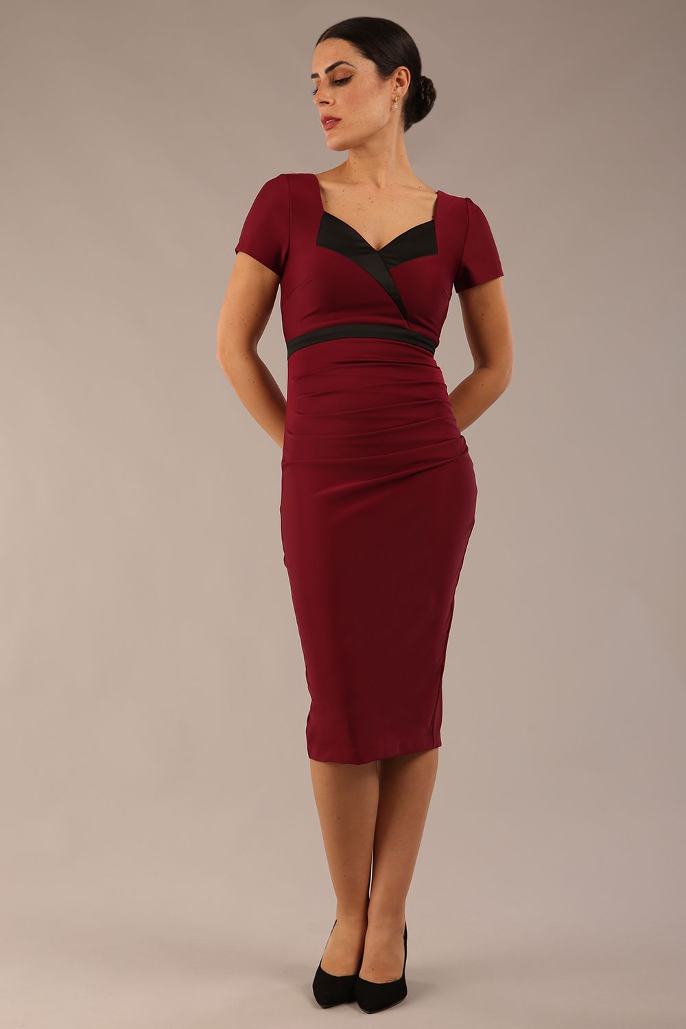 model is wearing a diva catwalk dress in burgundy with black satin detail contrast on the neckline and waistband short sleeves and pleating details with knee length