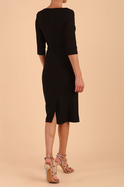 model wearing seed couture royale pencil skirt dress with pleating across the tummy area with rounded neckline with a split in the middle and 3 4 sleeve in Black colour front side