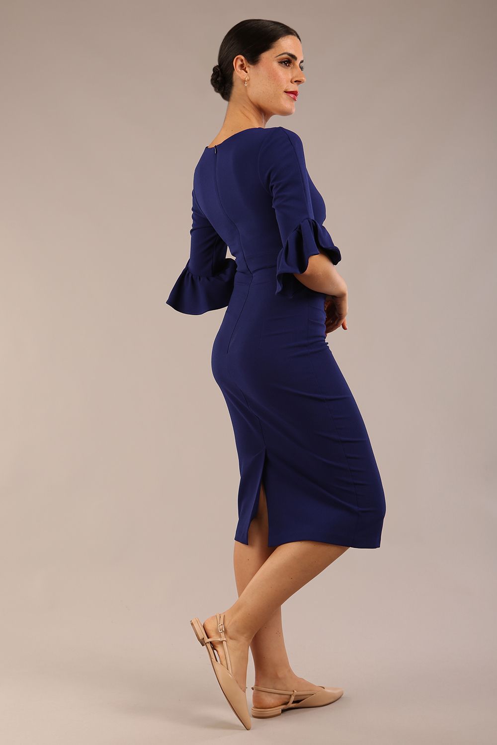 brunette model is wearing diva catwalk hollie pencil dress with frilled flute sleeve and low v-neck cut in oxford blue front side