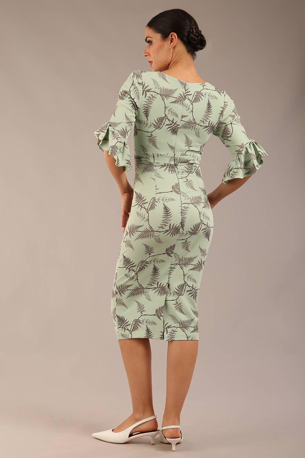 brunette model is wearing a diva catwalk hollie print pencil dress with 3/4 sleeves and frill details v neckline and knee length in deco green fern print front image