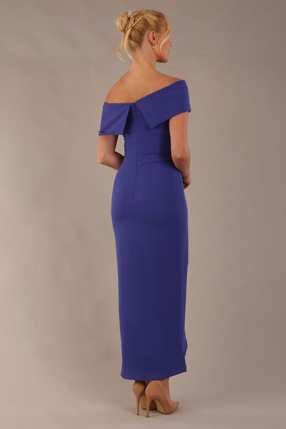 model wearing diva catwalk vegas calf length spectrum indigo midaxi dress with wide bardot neckline and open shoulders with a large opening at the front of the skirt with pleating coming down long skirt front (Spectrum Indigo)
