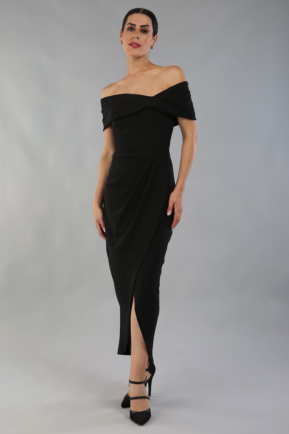 brunette model wearing diva catwalk vegas calf-length black midaxi dress with wide bardot neckline and open shoulders with a large opening at the front of the skirt with pleating coming down long skirt front (Black)