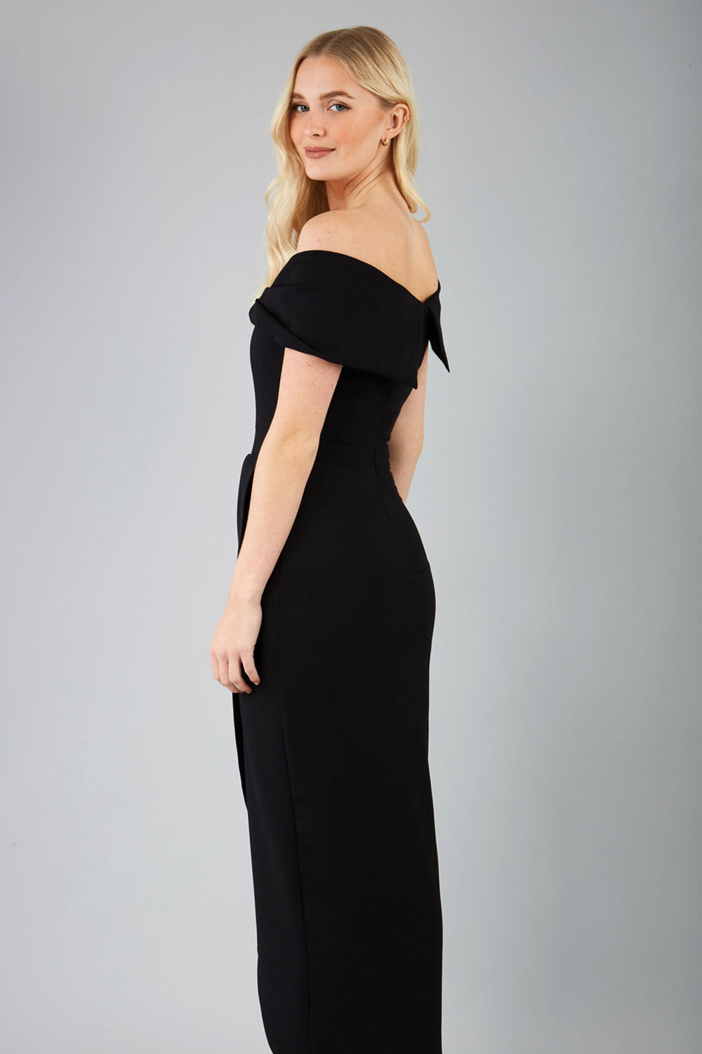 brunette model wearing diva catwalk vegas calf-length black midaxi dress with wide bardot neckline and open shoulders with a large opening at the front of the skirt with pleating coming down long skirt front (Black)
