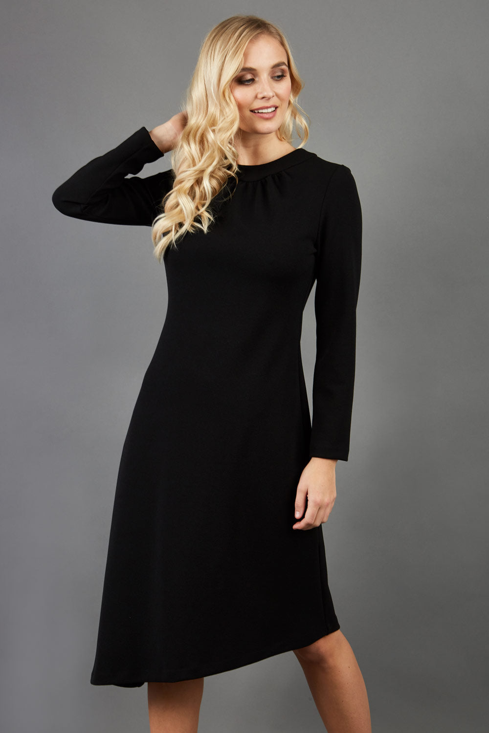 blonde model is wearing diva catwalk dartington asymmetric skirt midaxi long sleeve dress with rounded pleated neckline a-line style in black front
