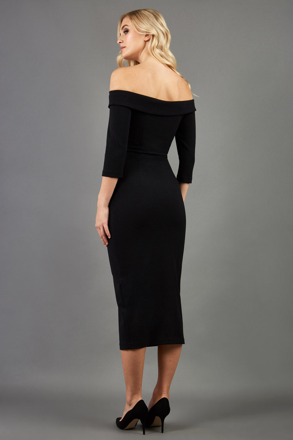 blonde model is wearing three quarter fitted dress off-shoulder with bardot neckline and buttons to front with pockets and vent on a skirt in black front