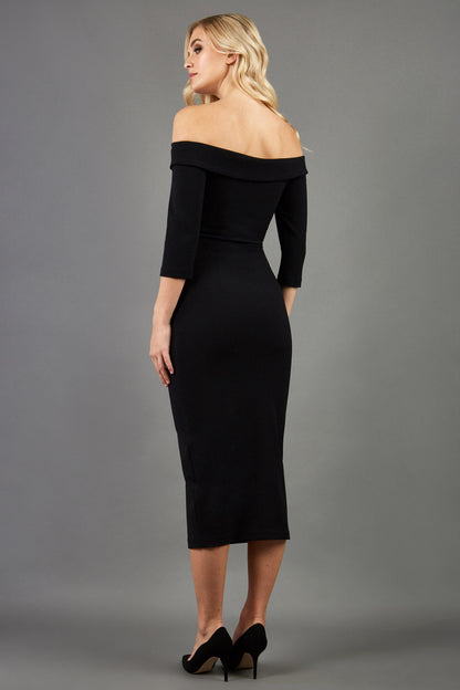 blonde model is wearing three quarter fitted dress off-shoulder with bardot neckline and buttons to front with pockets and vent on a skirt in black front