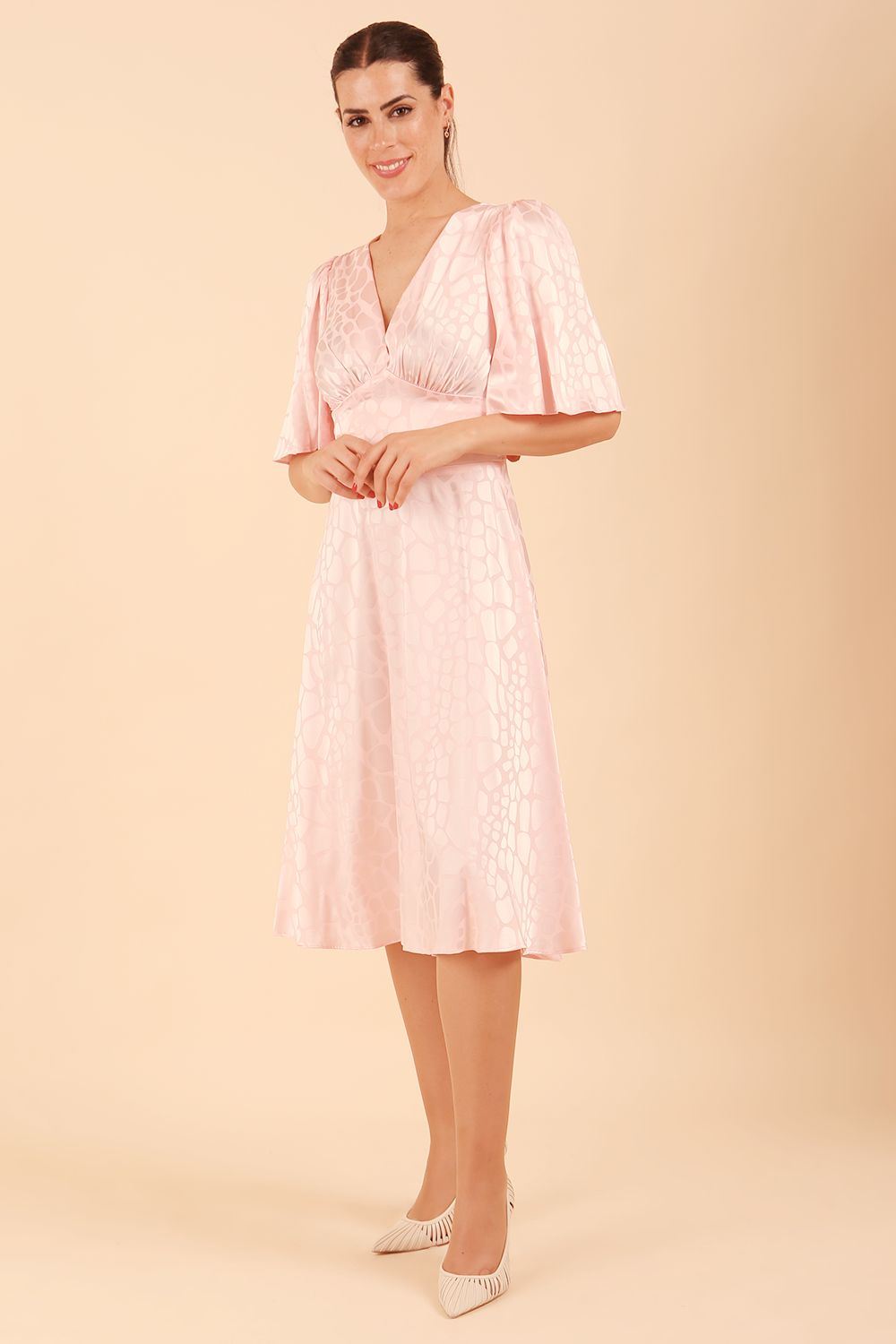 model wearing diva catwalk cambrian satin swing dress with bell short sleeve wide asymmetric waistband and pleating under bust in pink front